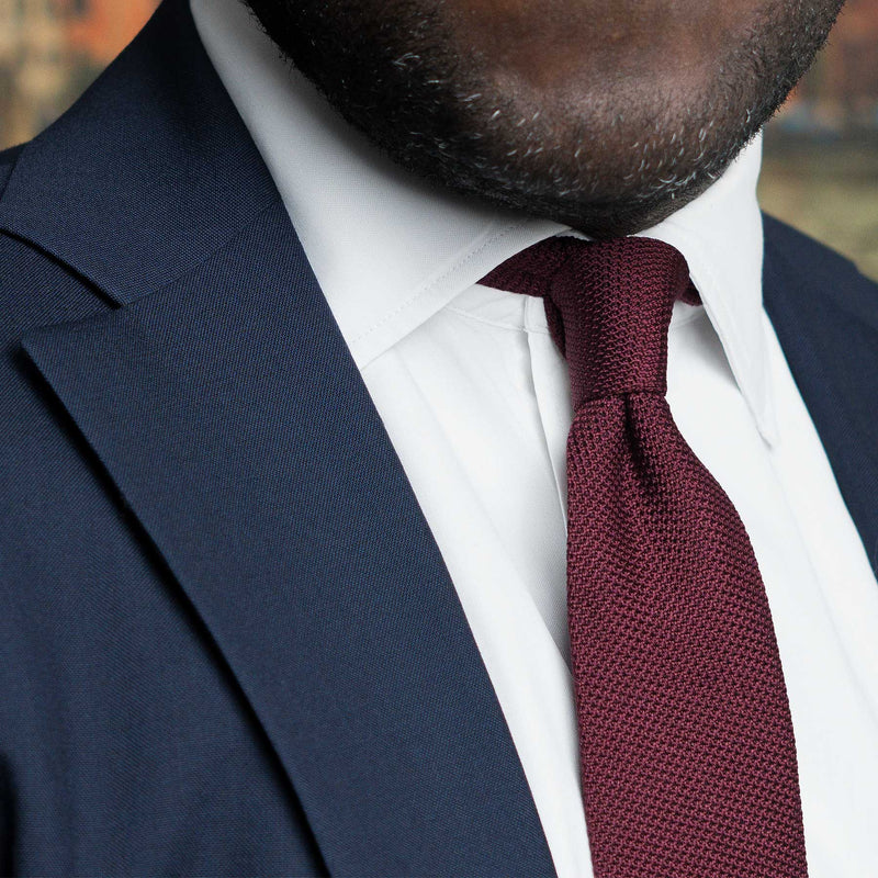 Burgundy grenadine tie paired with navy blue suit and white dress shirt.