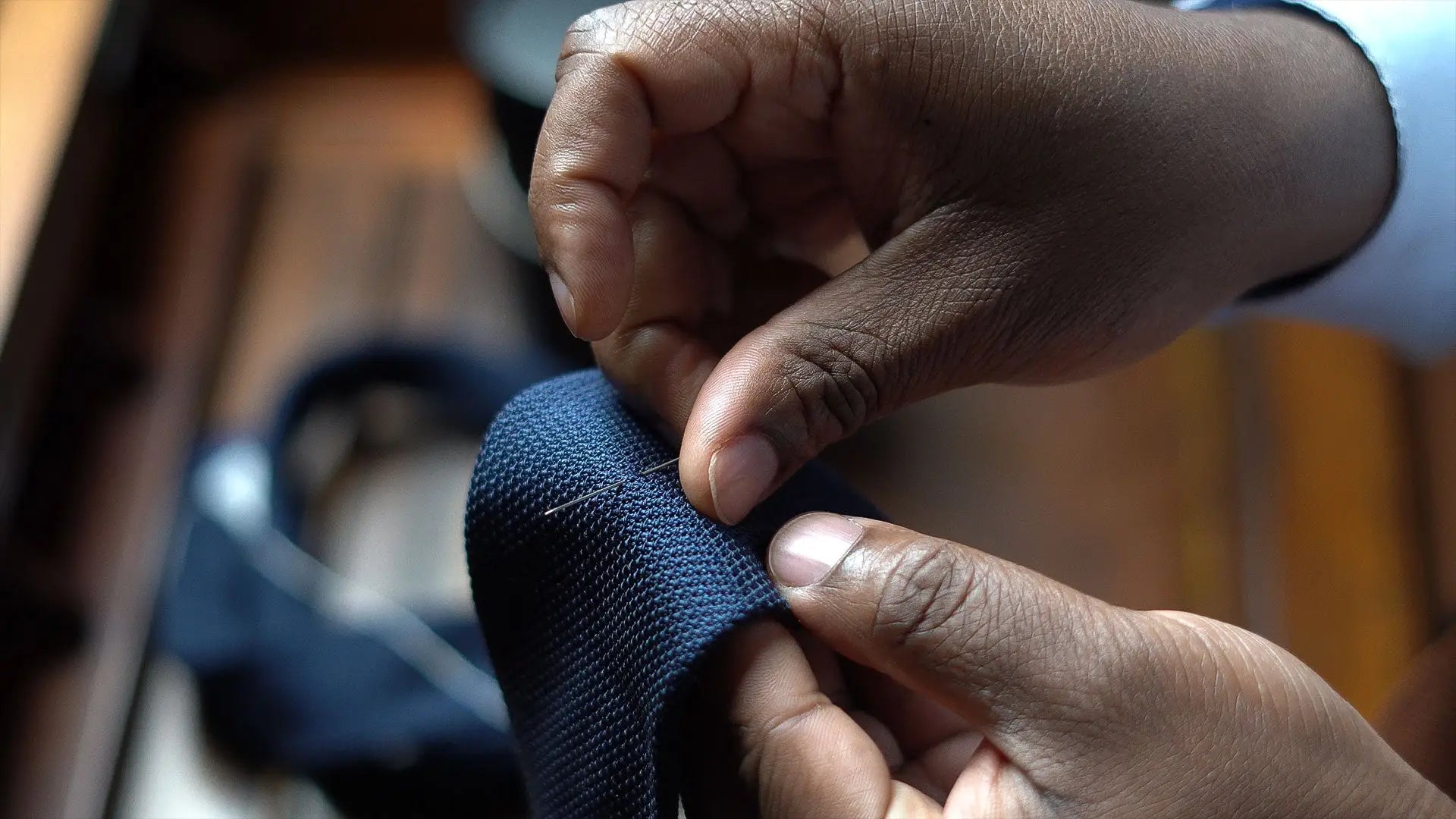 Hands stitching the edge of a navy grenadine tie