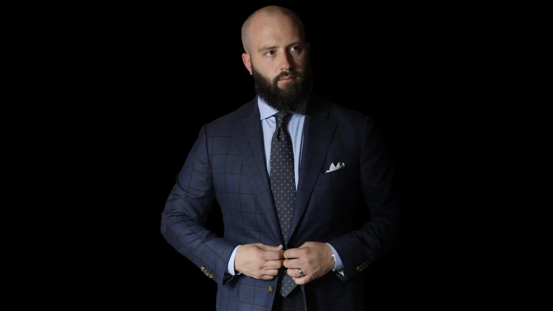 Man in a navy windowpane check suit with a light blue shirt, patterned tie and white pocket square