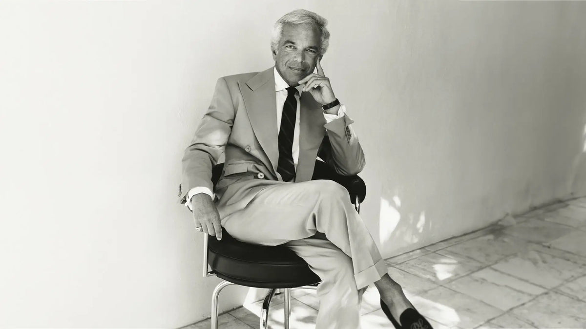 Black and white photograph of a man in a light suit and dark tie seated on a stool