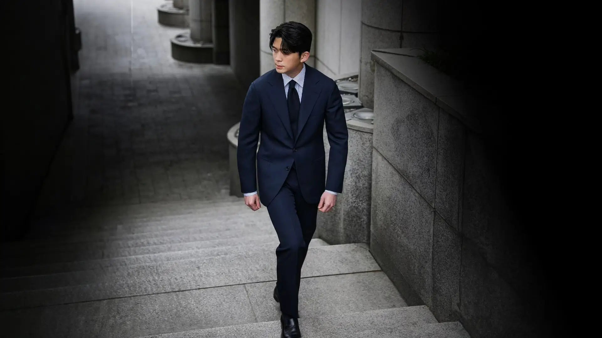 Man in a navy suit and navy tie walking down stone steps outside an office building