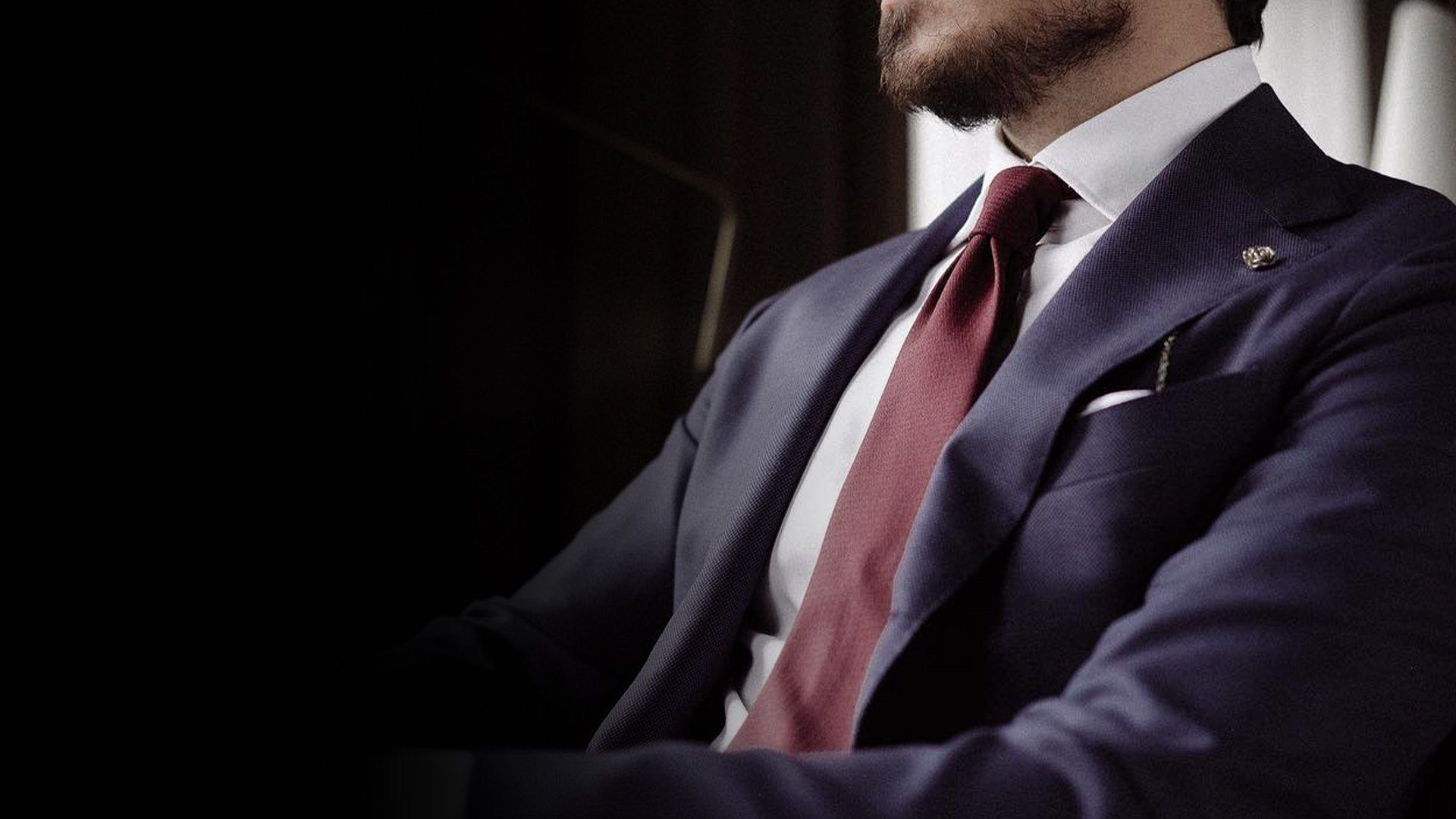 Burgundy tie worn with a navy blue suit, white shirt and white pocket square