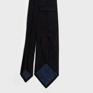 Close-up of black grenadine tie with detailed stitching and branded lining.