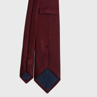 Close-up of burgundy grenadine tie with detailed stitching and branded lining.