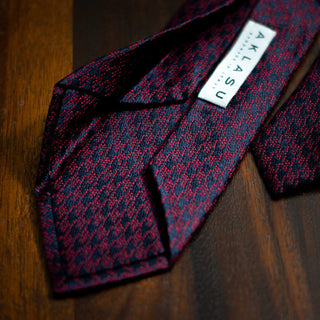 Detailed shot of Burgundy and Navy Houndstooth Silk Tie on wooden surface.