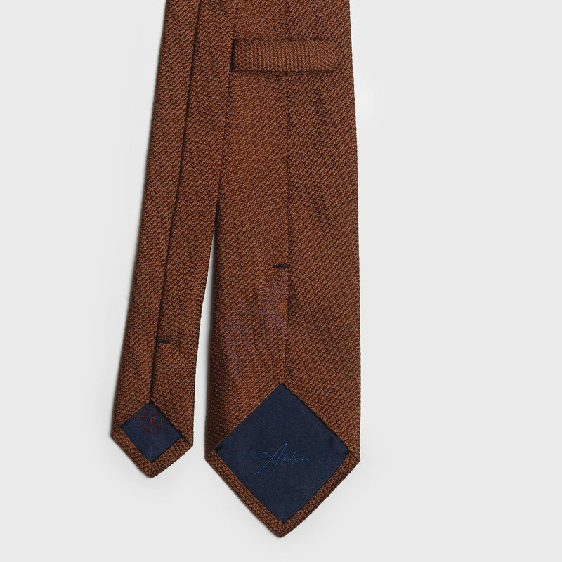 Back view of burnt orange grenadine tie with navy blue tipping and brand detail.