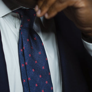 Dark blue floral grenadine tie with textured weave and subtle red floral pattern, worn with a suit.