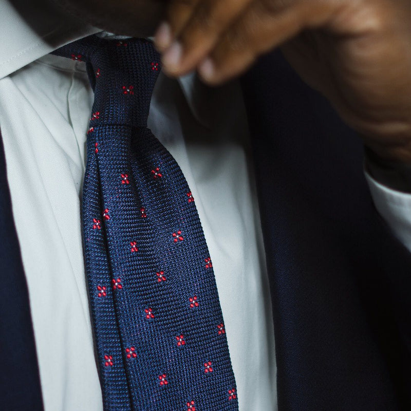 Dark blue floral grenadine tie with textured weave and subtle red floral pattern, worn with a suit.