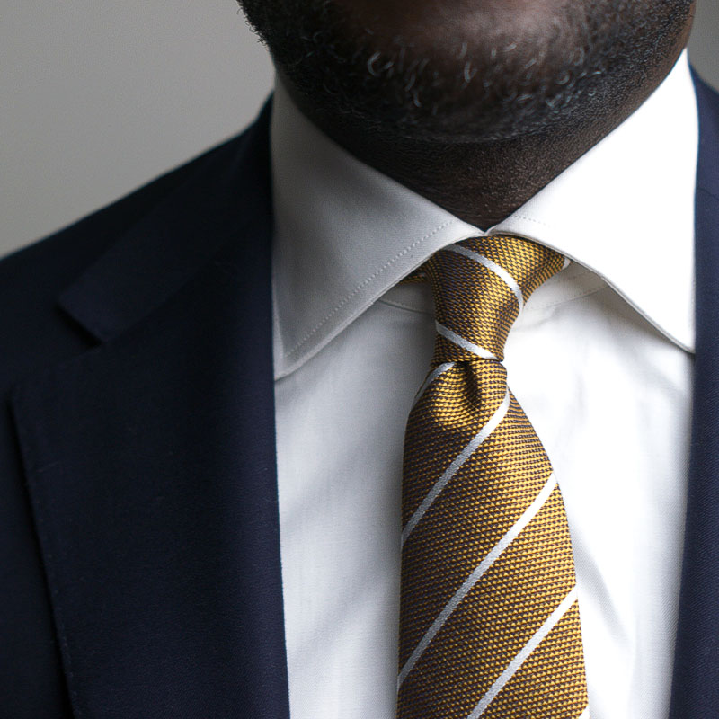 White striped metallic gold silk tie paired with a dark suit, showcasing elegance and sophistication.