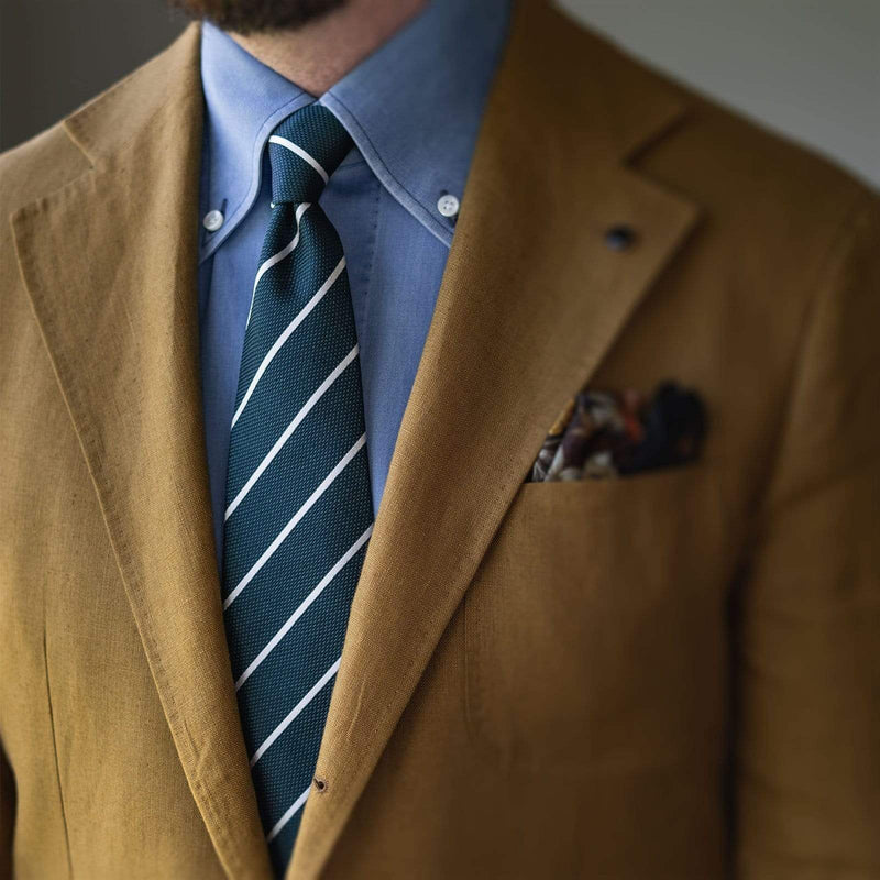 Man wearing emerald green silk tie with white stripes and a tan blazer.