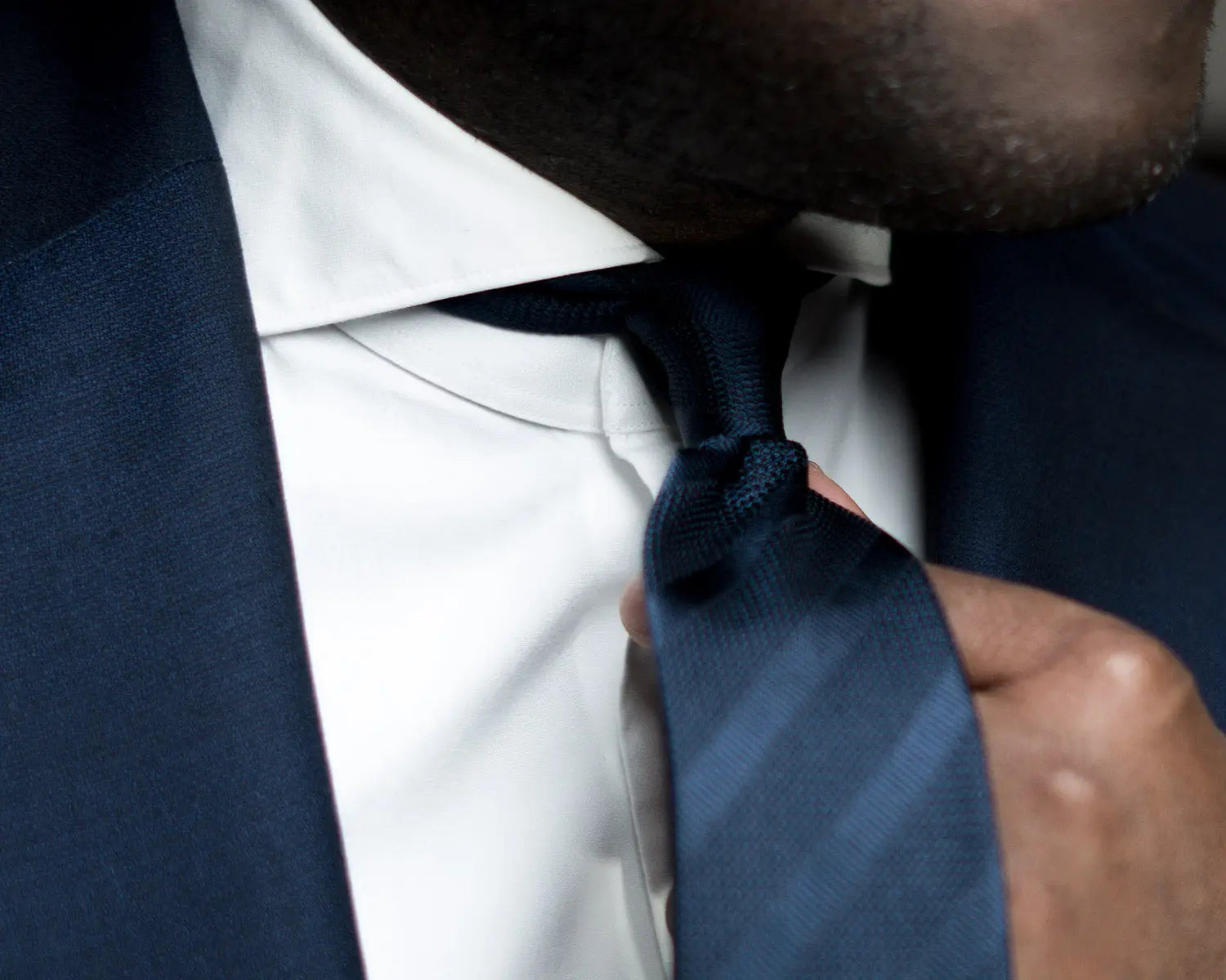 Man adjusting striped necktie showcasing shirt collar styles for timeless fashion