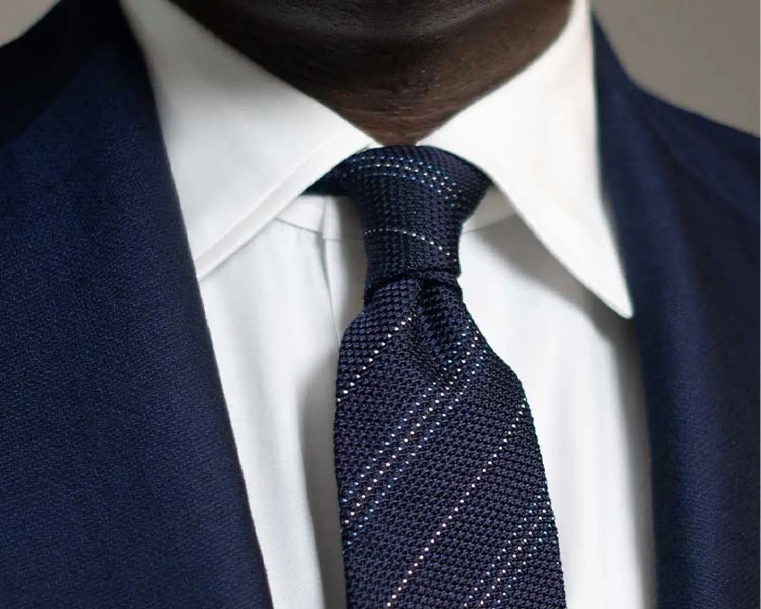 Navy knit tie with white stripes worn with a dress shirt, perfect for modern collar styles