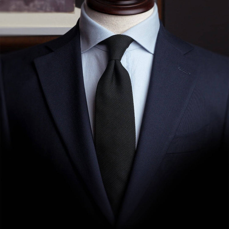 Black grenadine tie styled with a navy suit and light blue shirt for a polished look.