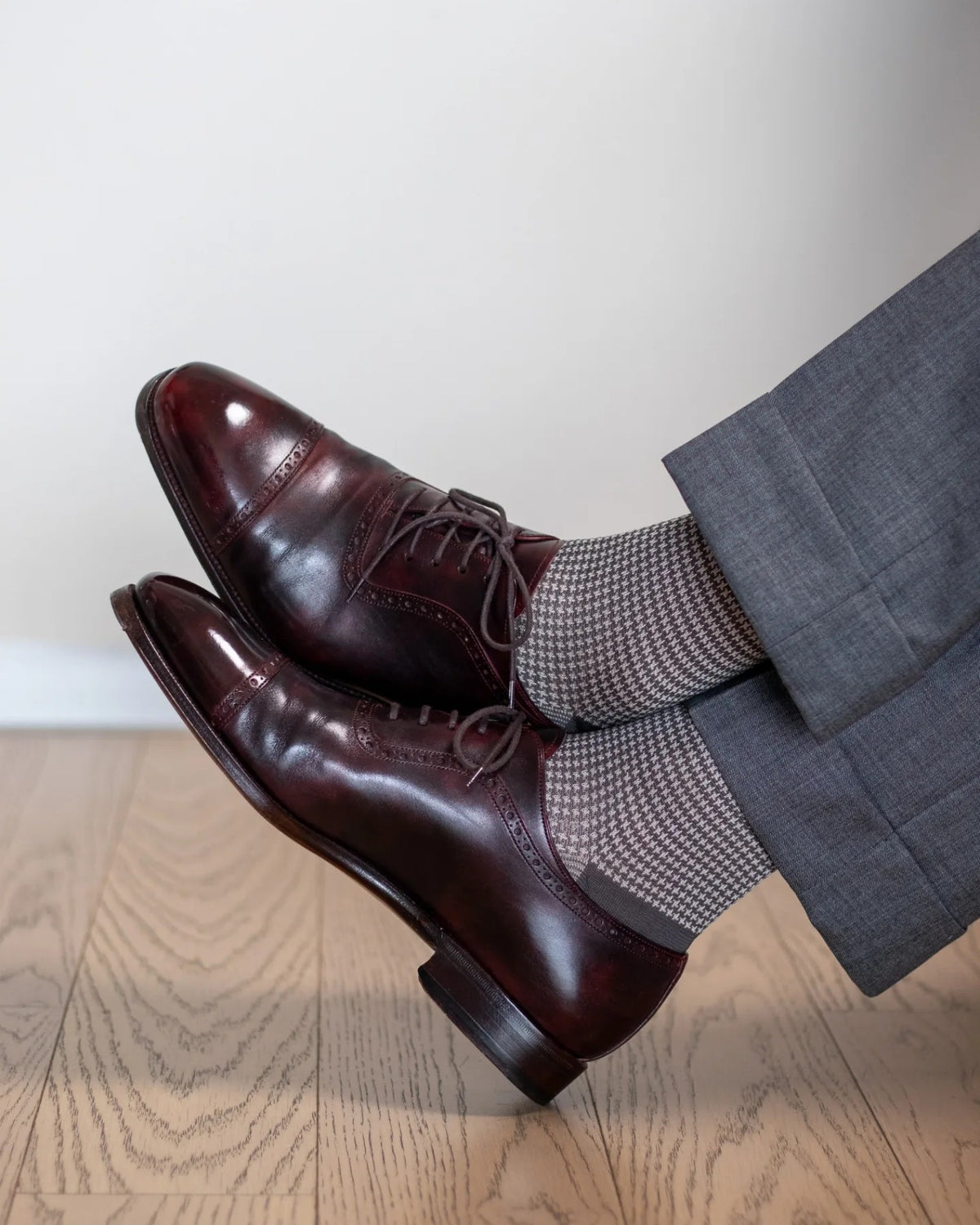 Grey houndstooth dress socks worn crossed at the ankle with burgundy brogues