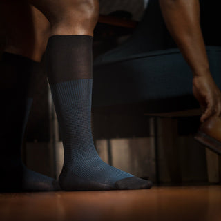 Man putting on shoes while wearing Blue and Black Houndstooth Dress Socks.