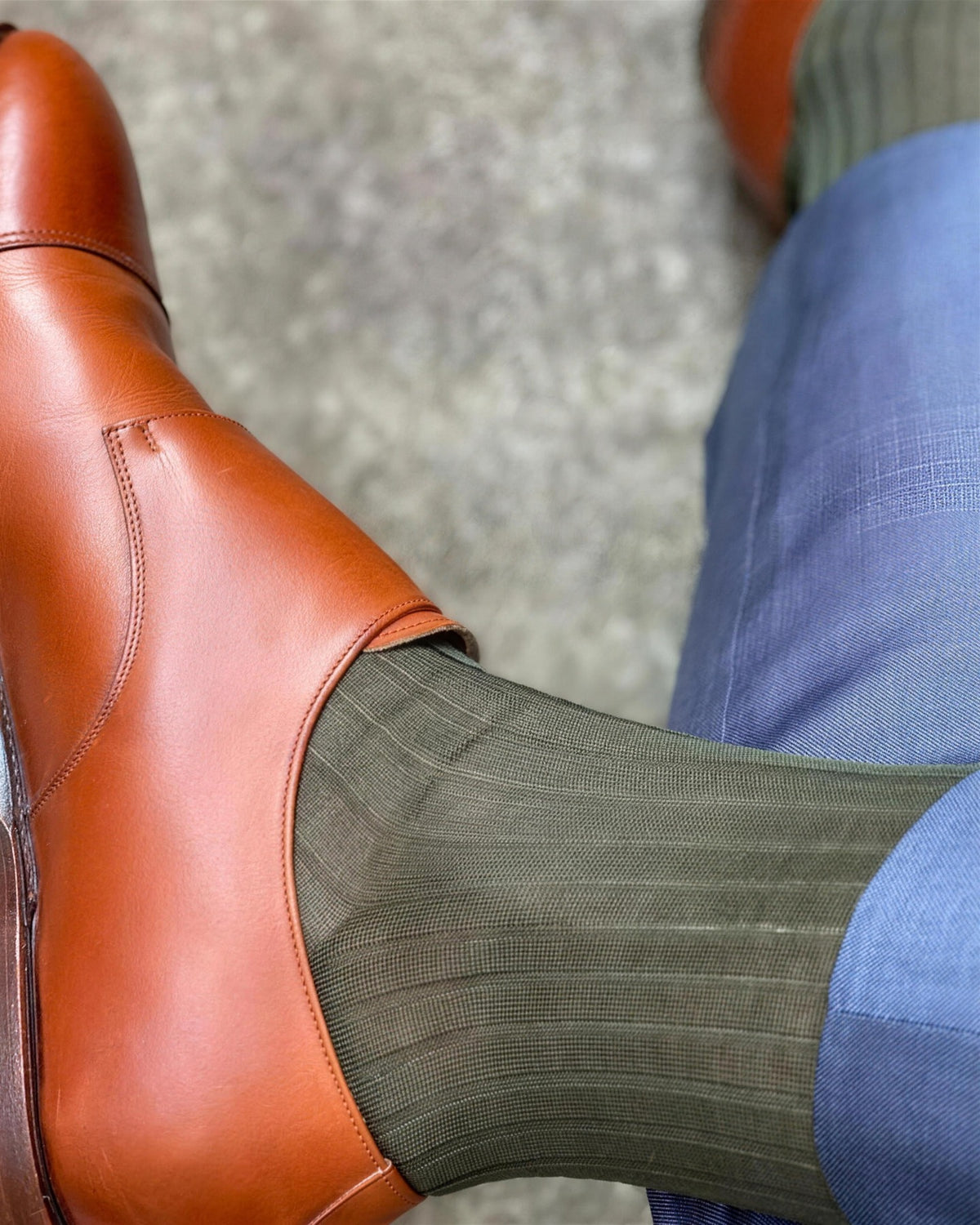Close view of olive green ribbed dress socks with a tan leather shoe and blue trousers