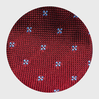 Close-up of red grenadine silk tie fabric with intricate blue floral pattern.